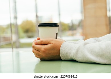 Two Hands Hold Coffee Cup. Warming Hands On Paper Coffee Hot Cup Mockup, Hugging Warm Mug In Cafe With Copy Space Side View