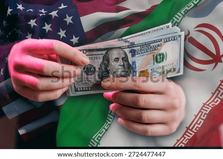 Two hands hold several one hundred dollar bills in front of flags representing the United States and Iran. The scene highlights themes of trade, currency, and international relations.