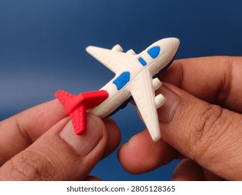 Two hands hold a small plastic white toy airplane with red and blue accents against a blue background.