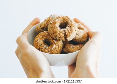 Two hands holding a bowl full of vegan donuts made of almond flour, banana, cinnamon and coconut flakes, with white background