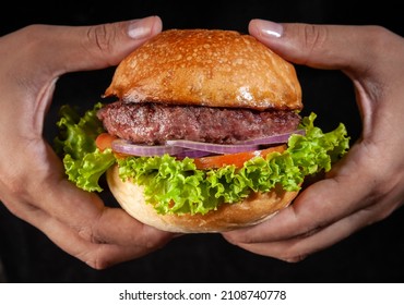 Two Hands Holding A Burger Sandwich, Lettuce, Onion, Tomato And Beef, In A Black Background