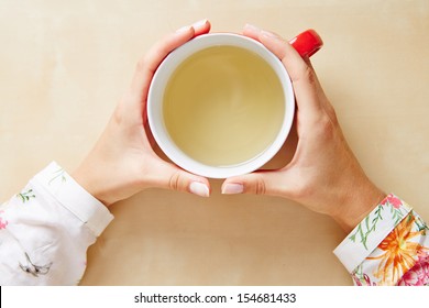 Two Hands Holding Chamomile Tea In A Cup From Above