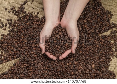 Two hands holding coffee beans, and mass of coffee around