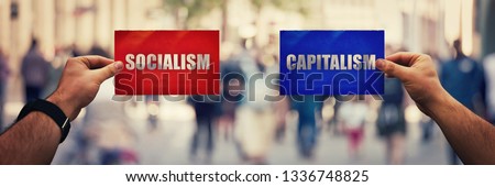 Two hands holding different colored paper sheet as socialist centralized economic planning versus capitalist liberated free market over crowded street background. Future strategy concept red vs blue.