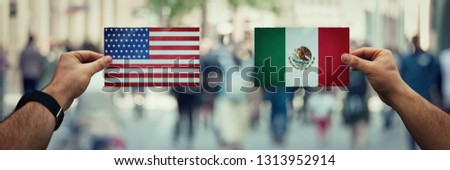 Two hands holding different flags, Mexico vs United States on politics arena over crowded street background. Future strategy, relations between countries. Cooperation or opposite conflict concept.