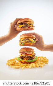 Two Hands Holding A Gourmet Cheese Burger On Top Of One Another With Beef Burger With Potato Chips On The Bottom 