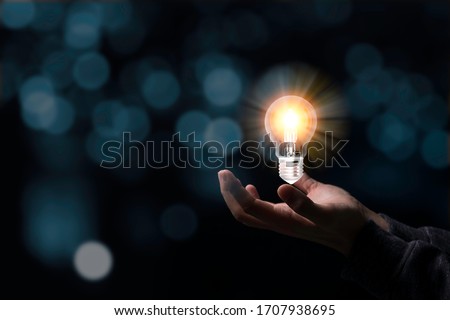 Two hands holding the light bulb that is illuminating. Creative protecting patents and ideas concept.