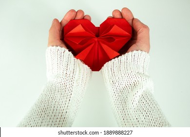 Two Hands Holding A Paper Origami Heart. Concept Of Love, Organ Donation, Charity, Kindness,  Insurance. Caring For Another Person, Giving To Others.