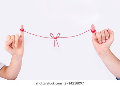 Two hands holding a red string tied in a bow to connect two people in a simple gesture of friendship or bond