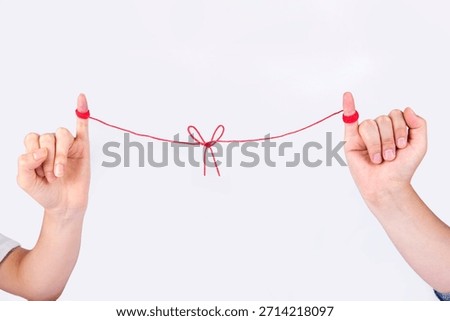 Two hands holding a red string tied in a bow to connect two people in a simple gesture of friendship or bond