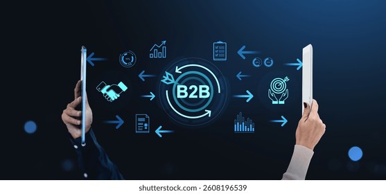 Two hands holding tablets with B2B symbols and digital data icons between them on dark background, representing business communication concept