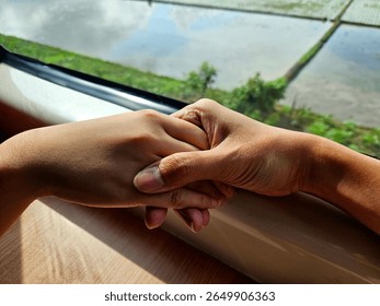 Two hands holding tenderly on train windowsill, capturing affection, connection, or farewell emotions