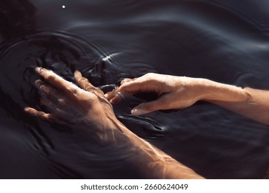 Two hands interact with the smooth surface of dark water, creating delicate ripples and reflections. setting sun casts a warm glow, enhancing the tranquil atmosphere.
