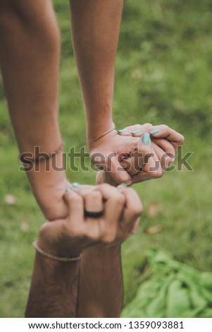 Two hands are intertwined in an equilibrium position of acroyoga. They have painted nails and they wear a ring and a bracelet.