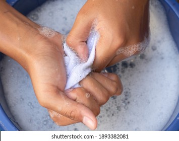 Two Hands Of Kid Wash Dirty White Socks Are Being Scrubbed In  Water Of The Detergent Or That Has Foamed And The Water Turns Black Child Learns To Clean By Self And Helps To Housework Of The Mother.