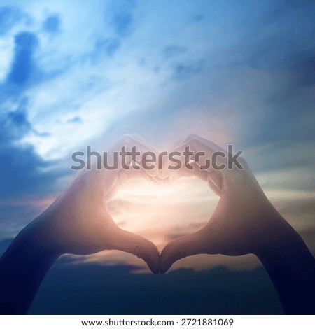 Two hands making a heart shape gesture against a beautiful sunset sky. Concept of love, hope, peace, faith, kindness, sharing, care, and support