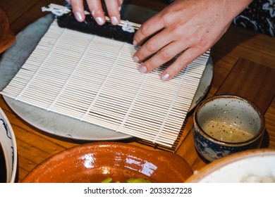 Two hands making a Japanese sushi roll.