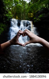 Two hands making a loveheart infront of a waterfall