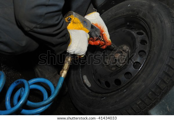 two hands making tyre fitting with air compressed\
wrench (screwing up bolts)