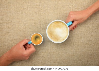 Two Hands, Man And Woman, Holding Small Espresso And Big Latte Cappuccino Coffee Cups Together Over Linen Canvas Background