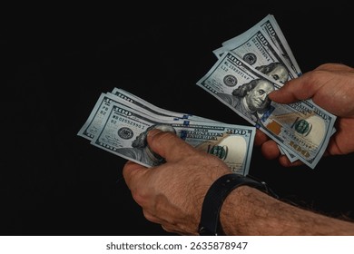 Two hands methodically count a stack of hundred dollar bills under low light, highlighting the texture and detail of the currency, creating a focused atmosphere.