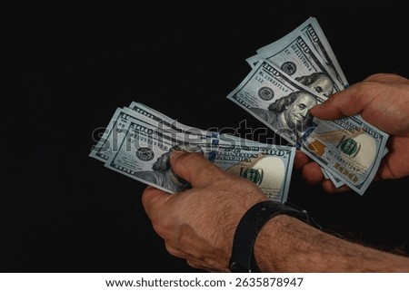 Two hands methodically count a stack of hundred dollar bills under low light, highlighting the texture and detail of the currency, creating a focused atmosphere.