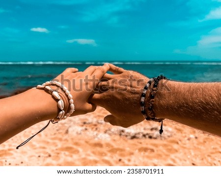 Two hands, one connection, and the endless expanse of the ocean beneath. A man's and a woman's hands, adorned with bracelets, intertwine above the horizon, symbolizing unity and love in Bali