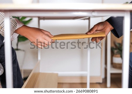 Two Hands Passing Yellow Envelope to Each Other Under Light Wooden Table, Bribery Concept