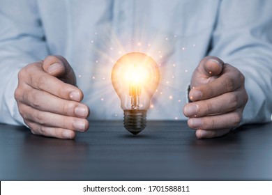 Two hands protecting the light bulb that is illuminating on the table. Creative protecting patents and ideas concept.