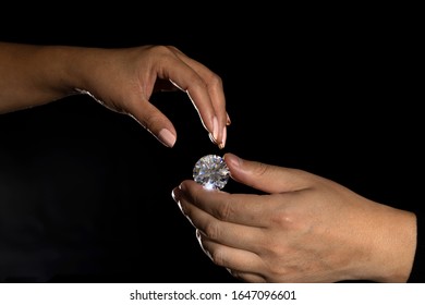 Two hands reaching for each other, a male hand holds diamond. Stock photo on black background.