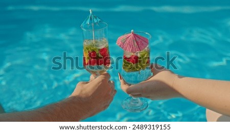 Two hands with refreshing drinks over the pools water surface on a hot summer day
