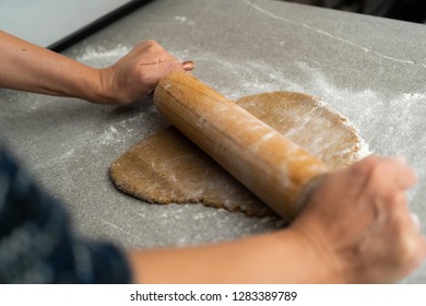 Two hands rolling, the biscuit dough evenly over flour with a rolling pin, making cookies and gingerbread in the kitchen for christmas