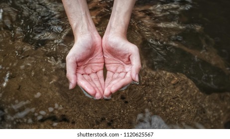 two hands are scooping clear fresh water from natural waterfall in forest for drinking