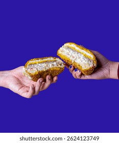 Two hands are seen holding halves of a creamy sandwich in front of a bold purple background. The sandwich reveals layers of chicken, sauce, and bread, suggesting a sense of shared food and connection