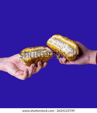 Two hands are seen holding halves of a creamy sandwich in front of a bold purple background. The sandwich reveals layers of chicken, sauce, and bread, suggesting a sense of shared food and connection