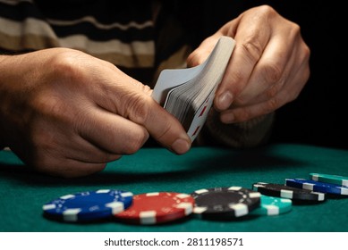 Two hands shuffle a deck of playing cards while chips rest on a green table. Players prepare for the next round of the card game. Focused attention surrounds the activity.