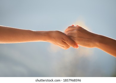 Two hands supporting each other, holding each other against the gentle blue natural background.