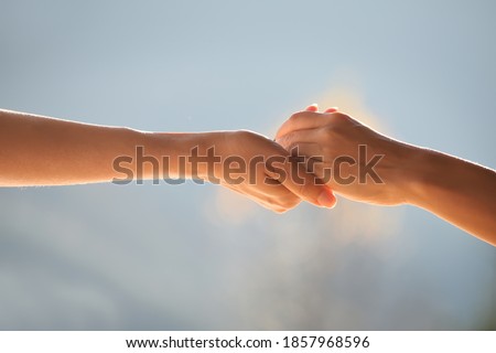 Two hands supporting each other, holding each other against the gentle blue natural background.