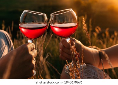 Two hands toasting red wine glasses. Toast and clinking glasses. Romantic dinner for a couple in love. Outdoor picnic in the grass in summer at sunset. the rays of the sun are reflected in the glasses - Powered by Shutterstock