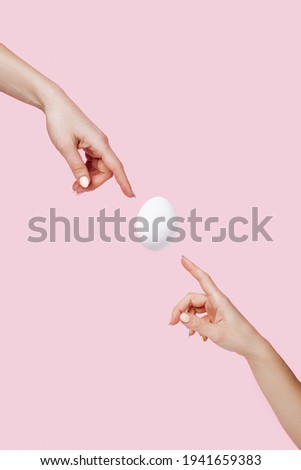 Two hands touching flying egg on pastel pink background. Creation of new life. Minimal Easter art concept.