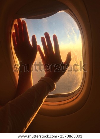 Two hands touching the window on the airplane looking at the golden hour as they fly home