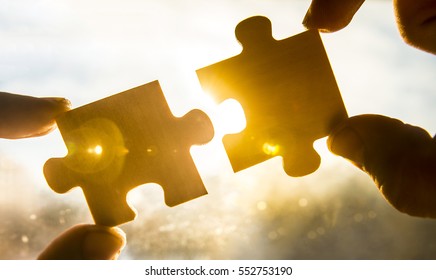 zwei Hände, die versuchen, ein paar Puzzleteil mit Sonnenuntergang zu verbinden. Jigsaw allein hölzernes Rätsel gegen Sonnenstrahlen. ein Teil des Ganzen. Vereinigungs- und Verbindungssymbol. Geschäftsstrategie. 