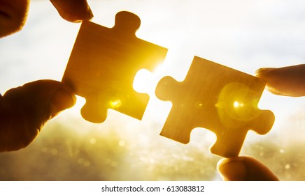 two hands trying to connect couple puzzle piece with sunset background. empty copy space. Jigsaw wooden puzzle against sun. one part of whole. symbol of association and connection. business strategy. 