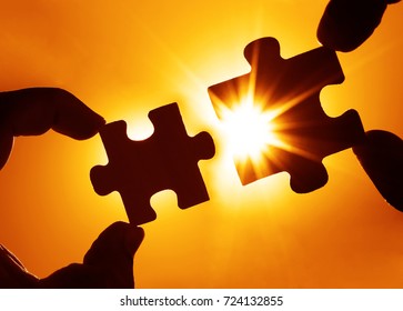 two hands trying to connect couple puzzle piece with sunset background. Jigsaw alone wooden puzzle against sun rays. one part of whole. symbol of association and connection. business strategy.