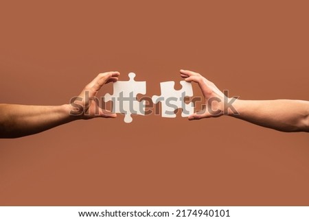 Two hands trying to connect couple puzzle piece on gray background. Teamwork concept. Closeup hand of connecting jigsaw puzzle.