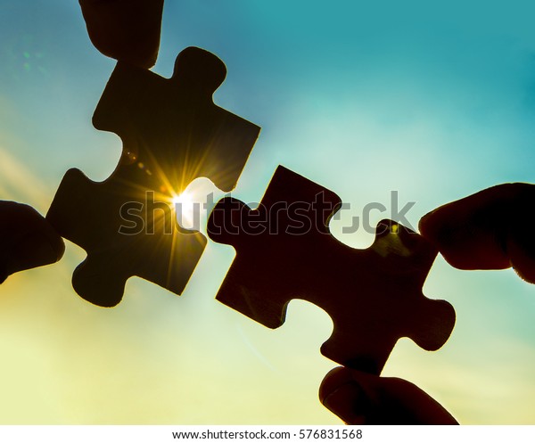 two hands trying to connect couple puzzle piece with sunset background. Jigsaw alone wooden puzzle against sun rays. one part of whole. symbol of association and connection. business strategy.