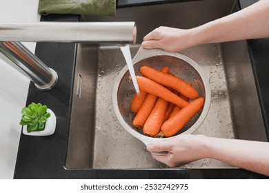 Two hands are washing bright orange carrots in a colander under running water, vegetable hygiene - Powered by Shutterstock