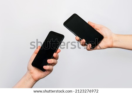 Two hands of two women holding mobile phones with blank black screens, empty copy space for design isolated on a gray background. Internet connection, File transfer, information exchange