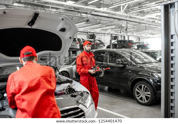 Two\
handsome auto mechanics in red uniform making wheel alignment with\
professional tools and computer at the car\
service