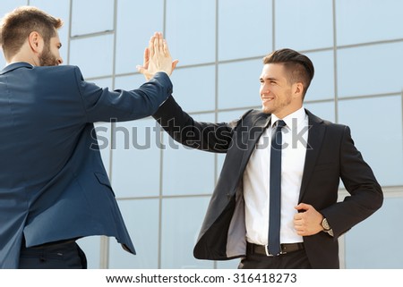 Two handsome business colleagues high fiving outdoors